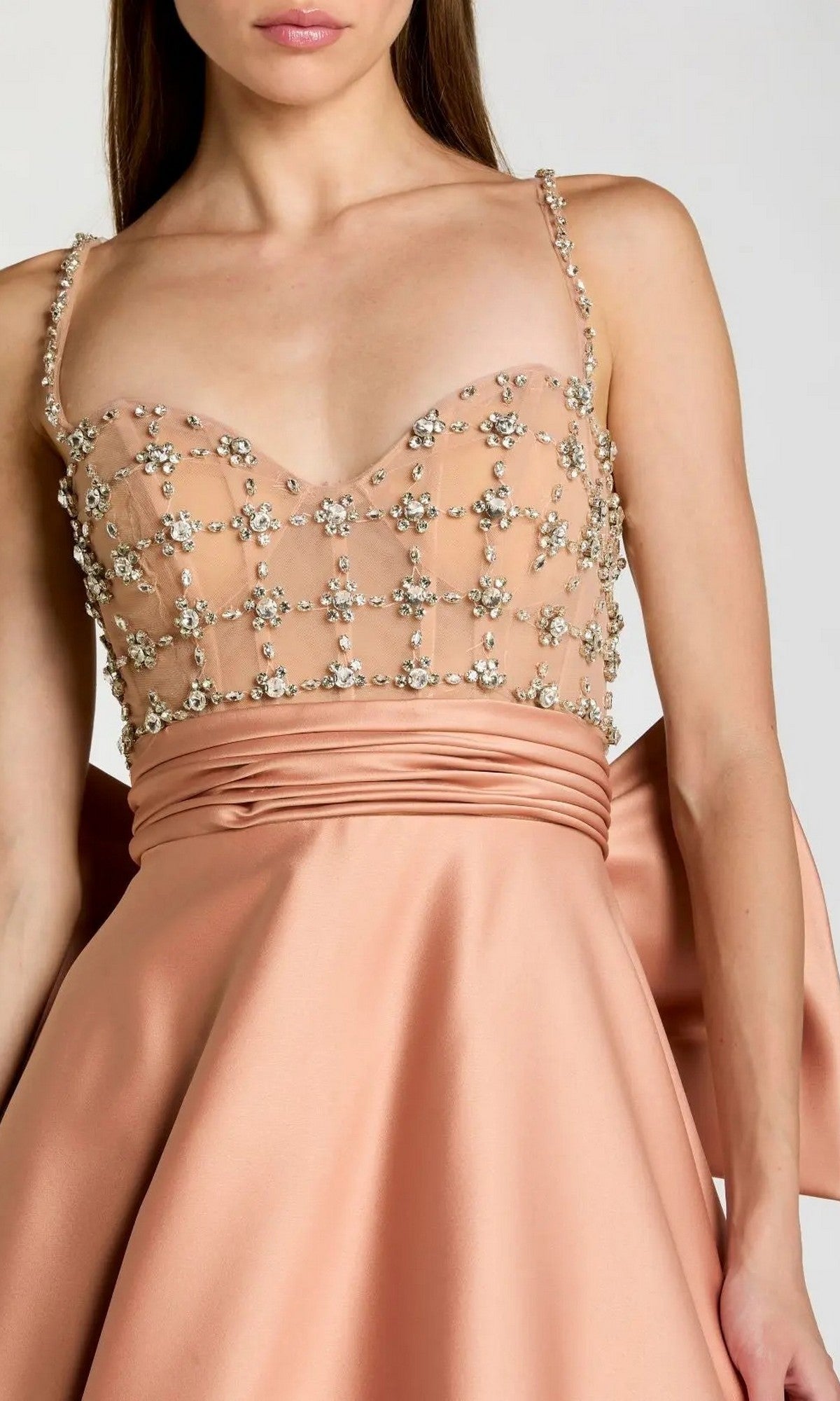 A woman wearing the Long Formal Dress: Mac Duggal 21242—a peach satin gown with a beaded mesh bodice, thin straps, and a large bow detail at the back—is photographed from the waist up.